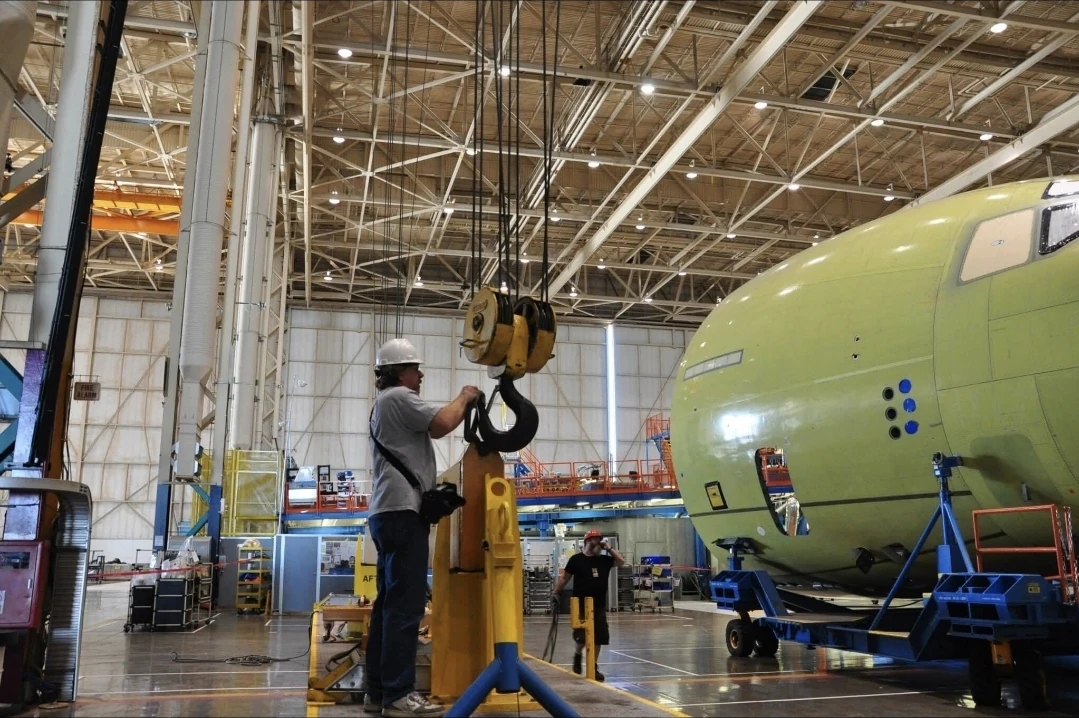 Technician operating a large crane hook to lift an aircraft component on the assembly floor